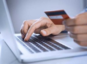 A person types on a laptop keyboard with one hand while holding a credit card in the other, indicating online shopping or payment.