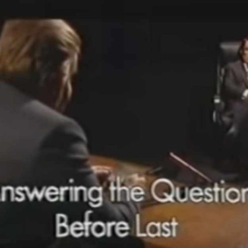 Two men sit facing each other in a dimly lit room with the words Answering the Question Before Last displayed.