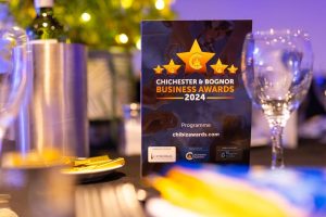 A Chichester & Bognor Business Awards 2024 programme rests on a decorated dining table set with glasses and cutlery.