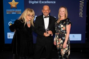 Three smartly dressed people smiling and holding a trophy at the Chichester & Bognor Business Awards 2024.