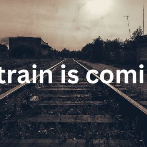 Railway tracks stretch into the distance at sunset with the words The train is coming.... centred across the image.