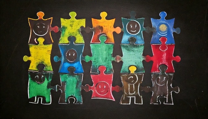 Colourful puzzle pieces with smiling faces drawn in chalk on a blackboard, representing diversity and unity.