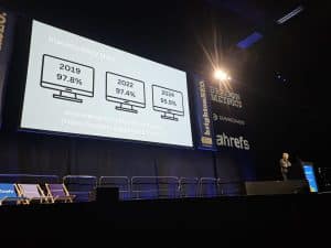 A presenter stands on a mostly empty stage, showing web accessibility statistics on a large screen at a conference.
